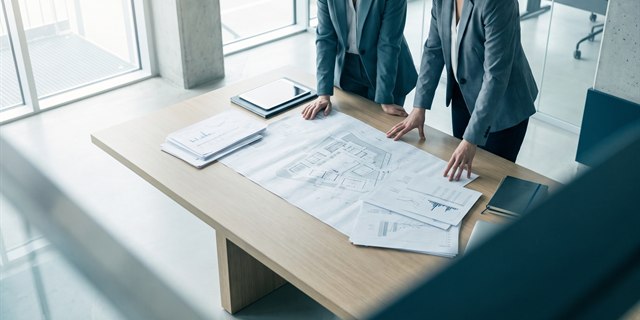 Two colleagues reviewing documents and a site plan across a table